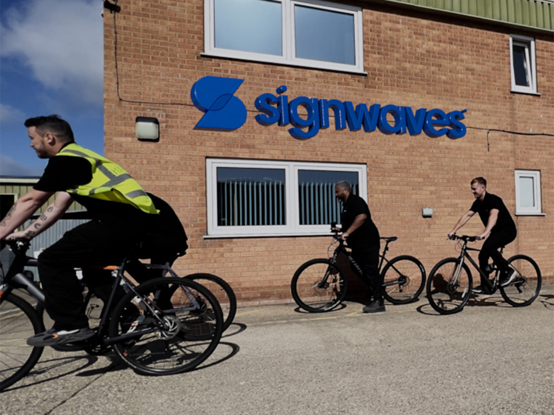 Signwaves employees on their bikes, cycling past Signwaves buildings