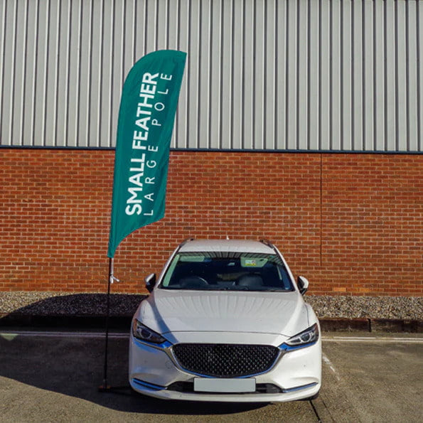 A tall teal feather flag banner with white text reading 'SMALL FEATHER LARGE POLE' next to a silver car.