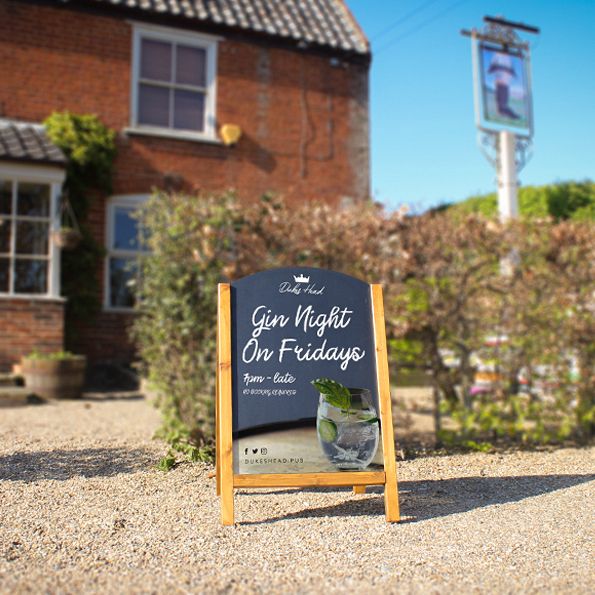Outdoor sign for Gin Night on Fridays in front of a brick building with greenery.
